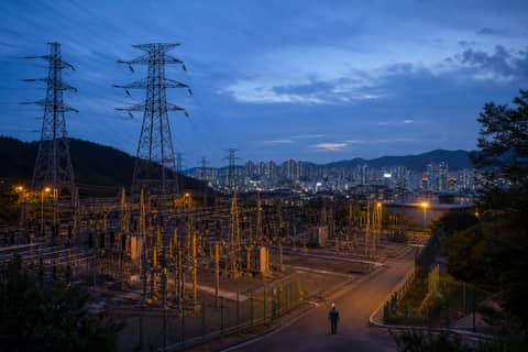 도시 외곽 변전소와 송전탑 사이를 걷는 작업자