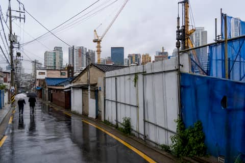재개발 구역 — 낡은 주택과 공사 가림막, 뒤로 타워크레인과 새 아파트