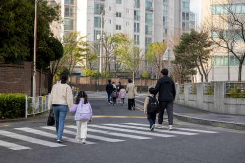 봄날 아파트 단지 앞 횡단보도를 건너 등교하는 아이와 부모들
