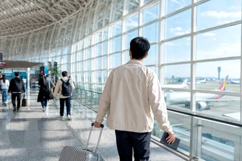 한낮의 공항 출국장에서 여권과 캐리어를 들고 창가를 지나는 여행자